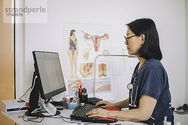 Seitenansicht eines weiblichen Gesundheitsexperten  der einen Computer am Schreibtisch im Krankenhaus benutzt