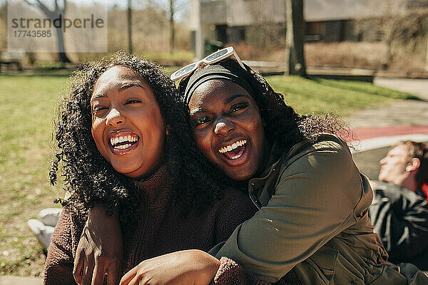 Porträt einer fröhlichen Frau  die ihre Freundin auf einem Spielplatz an einem sonnigen Tag umarmt