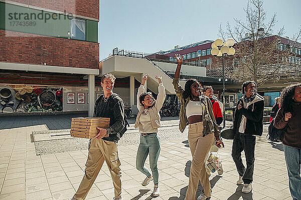 Glückliche multirassische Freunde winken mit den Händen  während sie auf der Straße an einem sonnigen Tag spazieren gehen