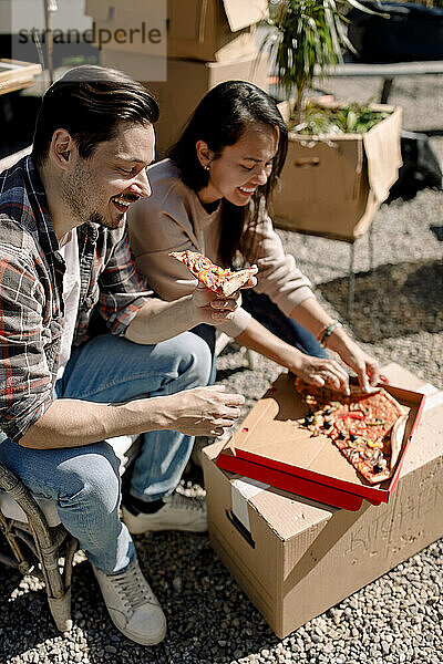 Lächelndes Paar beim Pizzaessen während des Umzugs in ein neues Haus