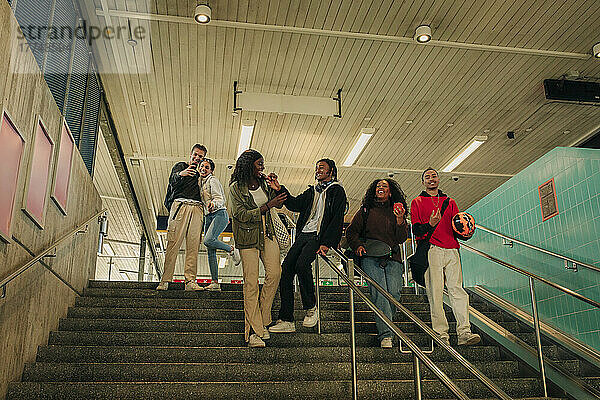 Männliche und weibliche Freunde  die sich auf den Stufen einer U-Bahn-Station vergnügen