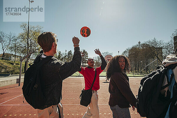 Männer spielen mit Ball  während sie mit Freunden auf einem Sportplatz an einem sonnigen Tag spazieren gehen