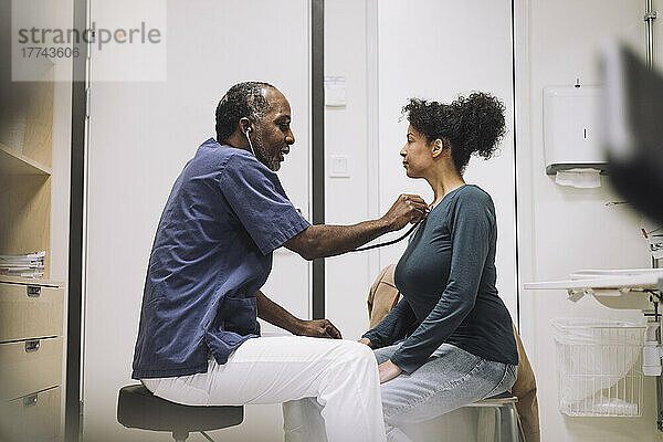 Männliches Pflegepersonal mit Stethoskop untersucht eine Patientin im Krankenhaus