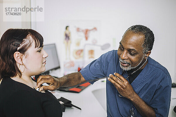Männlicher Gesundheitsexperte mit Stethoskop bei der Untersuchung einer Patientin in einer Klinik