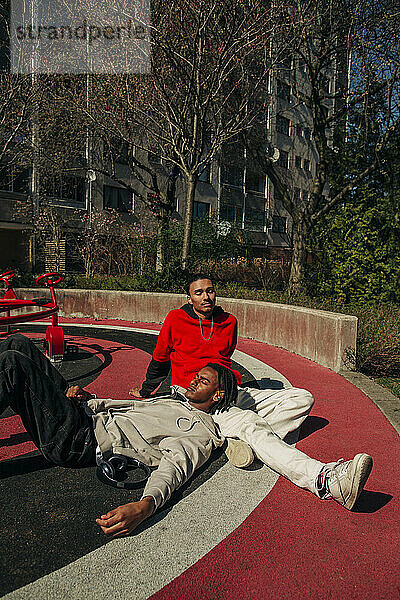 Mann entspannt sich auf dem Schoß eines Freundes auf einem Spielplatz an einem sonnigen Tag