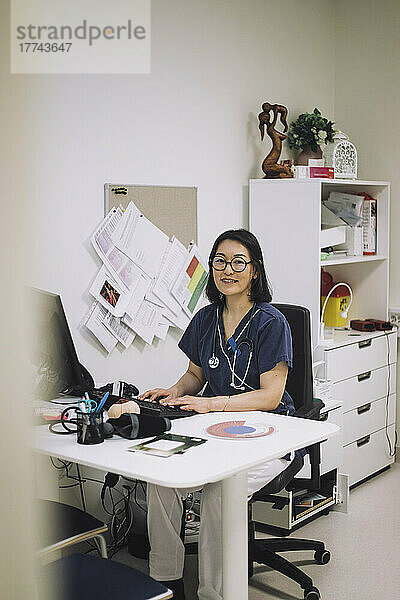 Porträt einer lächelnden Ärztin  die am Schreibtisch in einer medizinischen Klinik sitzt