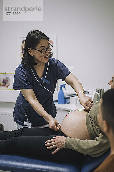 Lächelnde Ärztin misst den Bauch einer schwangeren Frau in einer medizinischen Klinik