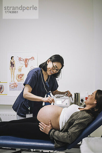 Lächelnder Gynäkologe bei der Ultraschalluntersuchung einer schwangeren Frau auf dem Untersuchungstisch im Krankenhaus