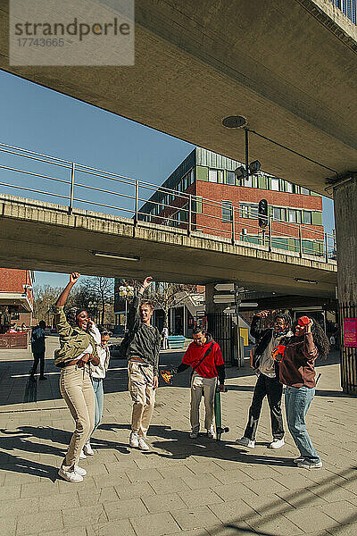Fröhliche multirassische Freunde tanzen unter einer Brücke an einer Straße an einem sonnigen Tag