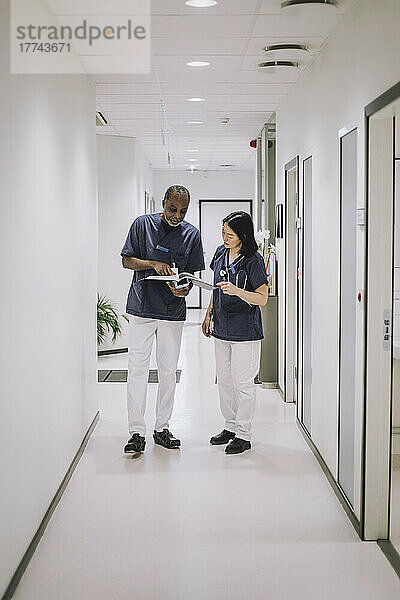 Männlicher Arzt bespricht in voller Länge einen Bericht mit einer Kollegin  während er im Krankenhaus auf dem Flur steht