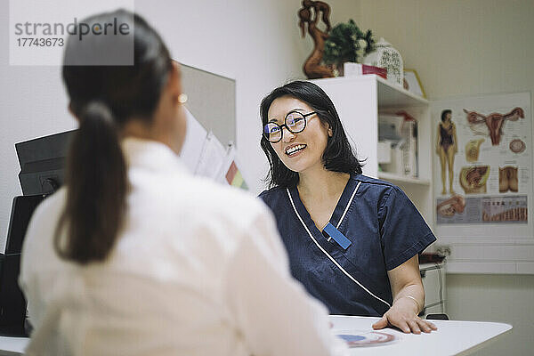 Glückliche Ärztin mit Brille im Gespräch mit einem Patienten in einer medizinischen Klinik