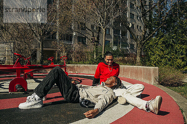 Lächelnde junge männliche Freunde verbringen ihre Freizeit auf einem Spielplatz an einem sonnigen Tag