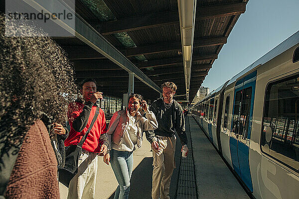 Multirassische spielerische Freunde stehen in der Nähe des Zuges am Bahnhof