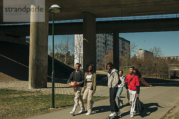 Multiracial männlichen und weiblichen Freunde zu Fuß zusammen auf der Straße während sonnigen Tag