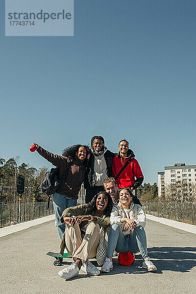 Glückliche multirassische Freunde  die sich auf dem Bahnsteig vor einem klaren blauen Himmel an einem sonnigen Tag amüsieren