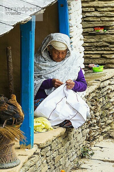 Ältere nepalesische Frau  die im Türrahmen sitzt und näht  Bergdorf Dhampus  Nepal  Asien