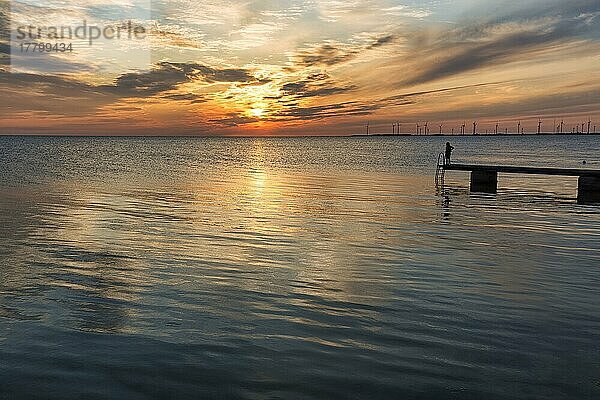 Person  Silhouette auf Badesteg am Meer  Windräder am Horizont  Abendhimmel bei Sonnenuntergang  Gegenlicht  Ostsee  Burgsvik  Insel Gotland  Schweden  Europa