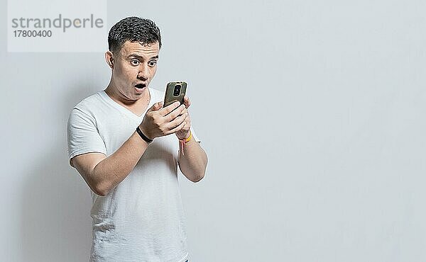 Gutaussehender Mann mit überraschtem Gesichtsausdruck mit seinem Telefon in der Hand  Eine erstaunte Person mit seinem Handy auf isoliertem Hintergrund