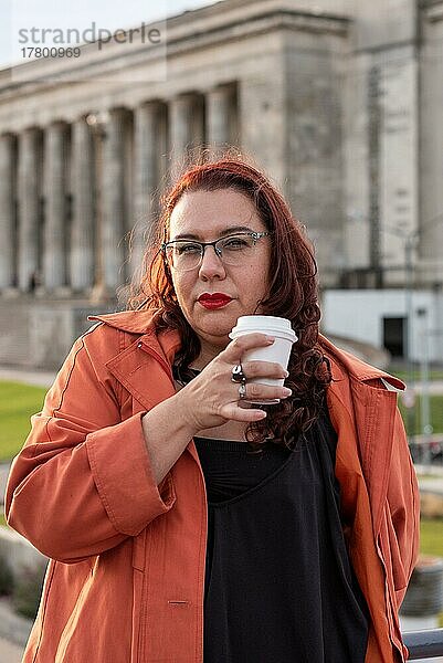 Porträt einer attraktiven Plus-Size-Frau  die in die Kamera schaut  während sie einen Kaffee in einer Universitätsumgebung trinkt