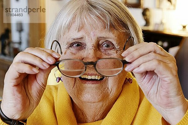 Seniorin setzt sich zuhause lächelnd die Brille auf  Bocholt  Nordrhein-Westfalen  Deutschland  Europa