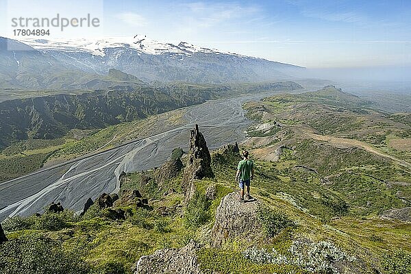 Wanderer blickt in die Ferne  Felsformationen am Gipfel Valahnúkur  Gletscherfluss Krossá in einem Bergtal  hinten Gletscher Eyjafjallajökull  wilde Natur  Isländisches Hochland  Þórsmörk  Suðurland  Island  Europa