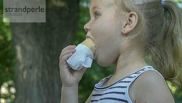 Süßes kleines Mädchen isst draußen Eis. Close-up-Porträt von blonden Mädchen sitzen auf Parkbank und essen Eis. Odessa  Ukraine  Europa