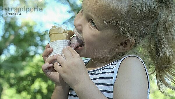 Süßes kleines Mädchen isst draußen Eis. Close-up-Porträt von blonden Mädchen sitzen auf Parkbank und essen Eis. Odessa Ukraine