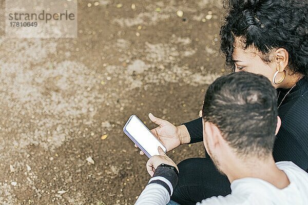 Hände von zwei Teenagern  die auf den Handy-Bildschirm zeigen  Zwei Teenager sitzen und zeigen auf einen leeren Handy-Bildschirm mit Platz für Text. Zwei Freunde beobachten Fotos und zeigen auf den Handy-Bildschirm