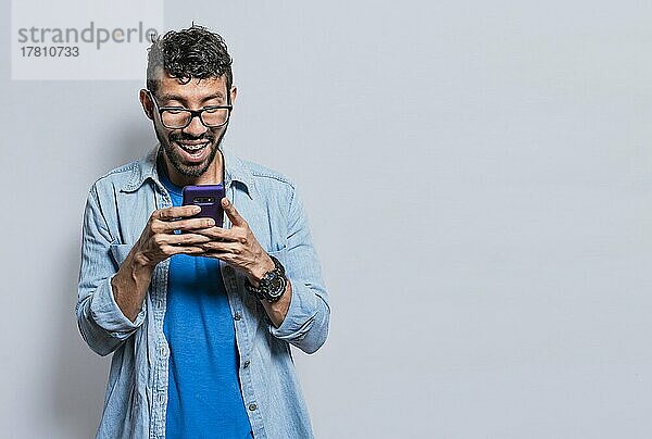Lächelnd gut aussehend Junge SMS mit seinem Handy isoliert  junge lateinische Mann glücklich mit seinem Handy isoliert  glücklich Teenager SMS mit seinem Handy