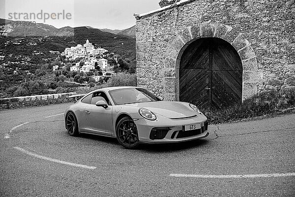 Nachgestellte Aufnahme von klassisches Schwarz-Weiß Foto von Porsche 911 an historischer Streckenabschnitt von Rallye Monte Carlo 1965 mit moderner Supercar Sportwagen Porsche GT3  im Hintergrund La Roquette-sur-Var  Département Alpes-Maritimes  Region Provence-Alpes-Côte d?Azur  Frankreich  Europa