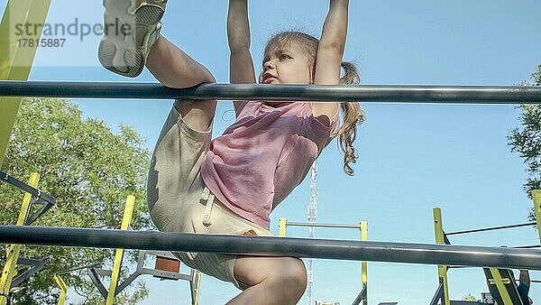 Kleines Mädchen klettert Gymnastikleiter auf offenen Sportplatz im Freien. Nettes kleines Mädchen krabbelt auf vertikale Sportleiter in Stadtpark auf Sonne Tag. Odessa  Ukraine  Europa