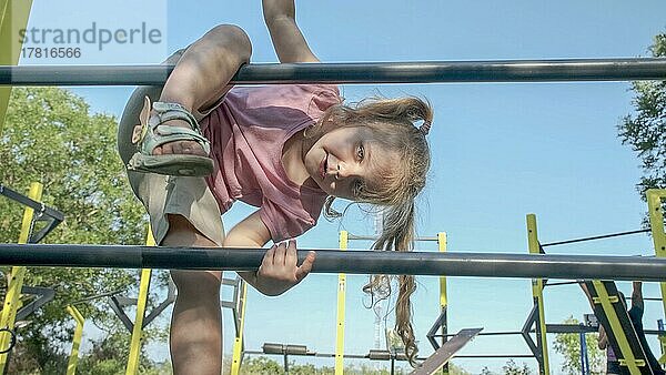 Kleines Mädchen klettert Gymnastikleiter auf offenen Sportplatz im Freien. Nettes kleines Mädchen krabbelt auf vertikale Sportleiter in Stadtpark auf Sonne Tag. Odessa  Ukraine  Europa