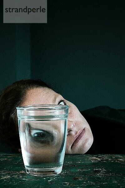 Gruseliges Gesicht einer Frau  Auge gespiegelt in einem Wasserglas