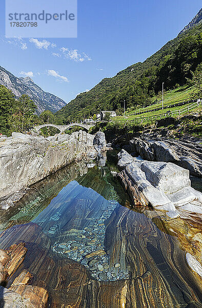 Schweiz  Tessin  Lavertezzo  Fluss Verzasca  der im Sommer durch das Valle Verzasca fließt  mit der Bogenbrücke Ponte dei Salti im Hintergrund