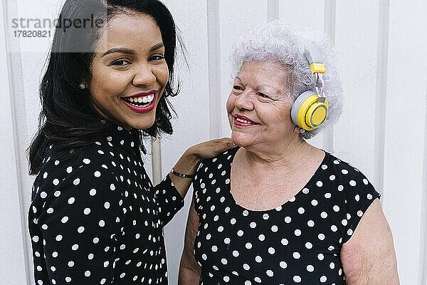 Glückliche Seniorin mit kabellosen Kopfhörern blickt ihre Tochter an