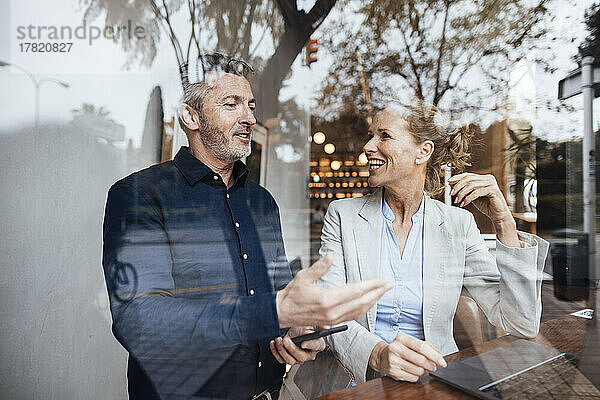 Lächelnder Geschäftsmann im Gespräch mit Geschäftsfrau im Café  gesehen durch Glas