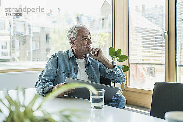 Nachdenklicher älterer Geschäftsmann mit der Hand am Kinn im Büro