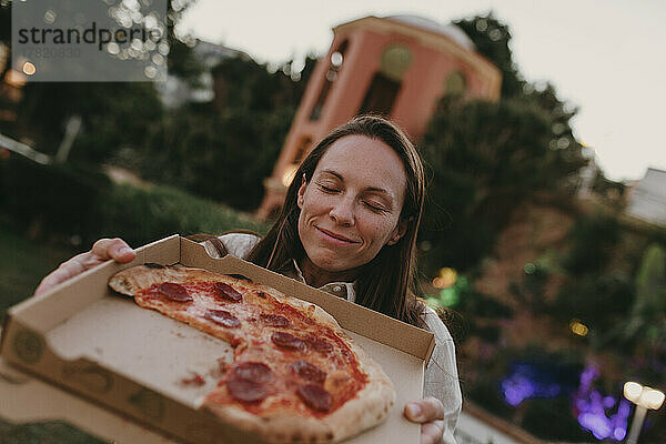 Frau mit geschlossenen Augen zeigt Pizza im Karton