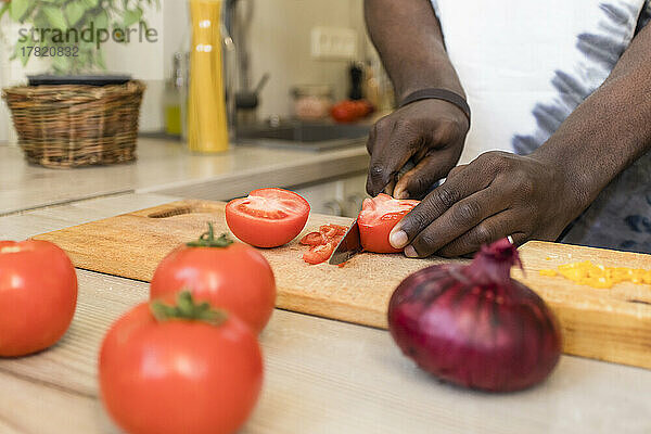Hände eines Mannes  der in der Küche Tomaten schneidet