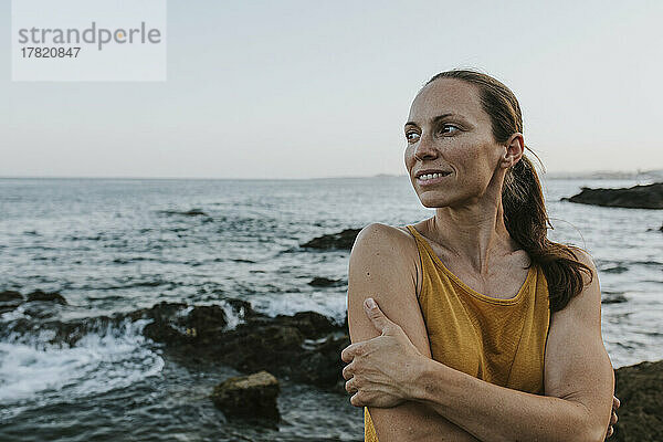 Glückliche Frau umarmt sich am Meeresufer bei Sonnenuntergang