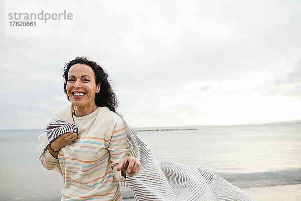 Glückliche Frau mit Schal  die vor dem Meer steht