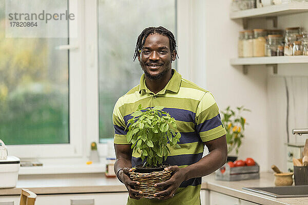 Smiling man holding basil plant standing in kitchen