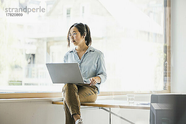 Geschäftsfrau mit Laptop sitzt am Schreibtisch am Fenster