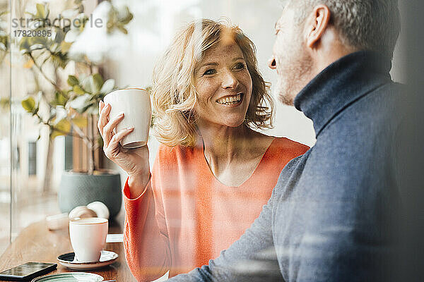 Glückliche Frau hält Kaffeetasse und spricht mit Mann im Café