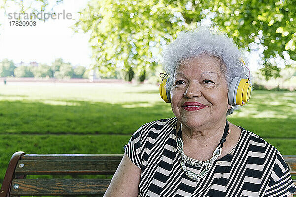 Glückliche ältere Frau mit kabellosen Kopfhörern  die im Park Musik hört