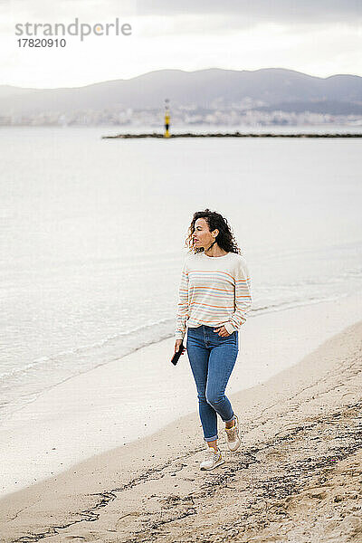 Reife Frau mit Handy geht am Strand spazieren
