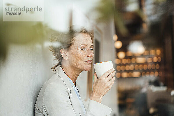 Geschäftsfrau trinkt Kaffee im Café  gesehen durch Glas