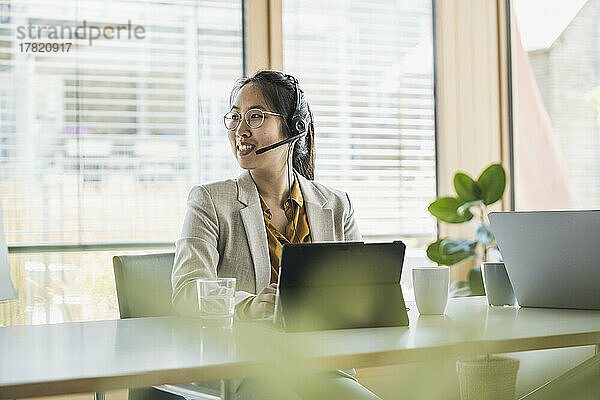 Glückliche Geschäftsfrau mit Tablet-PC sitzt am Arbeitsplatz