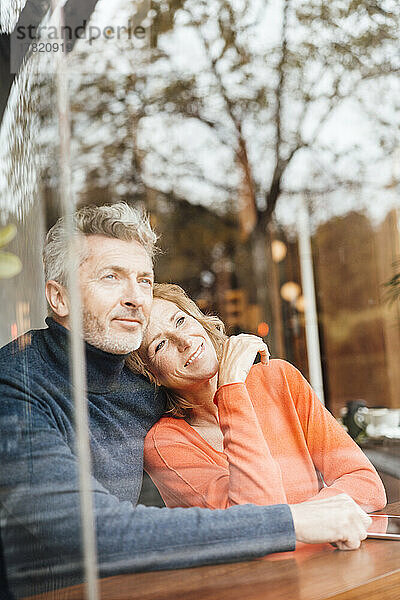 Lächelnder Mann umarmt Frau  die im Café sitzt und durch Glas gesehen wird
