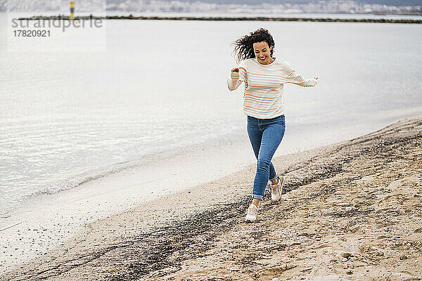 Fröhliche Frau läuft am Strand auf Sand